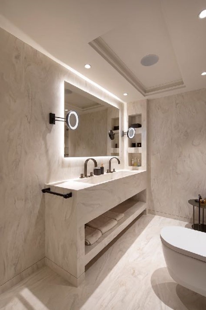 Rivestimento di pavimenti e pareti, mobile con lavabo, portasciugamani e nicchie integrati in Corian<sup>®</sup> Carrara Cream  (a sinistra). Dietro la vasca, parete rivestita in Corian<sup>®</sup> Smoke Drift Prima, completata da illuminazione a scomparsa. Design Soliform; immagini © Dian Stanchev, tutti i diritti riservati.